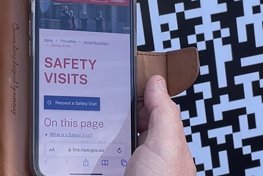 phone displaying "safety visit" screen on FRNSW website with QR code in background