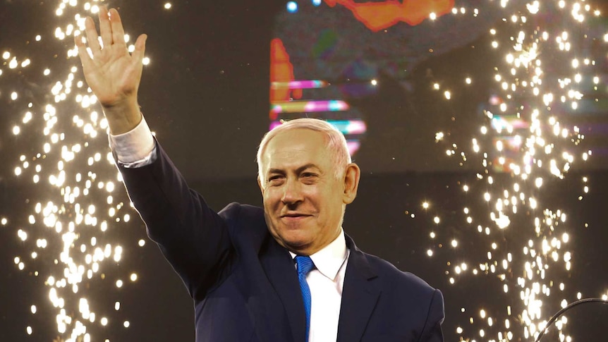 Israel's Prime Minister Benjamin Netanyahu waves to supporters on stage as fireworks fire behind him.