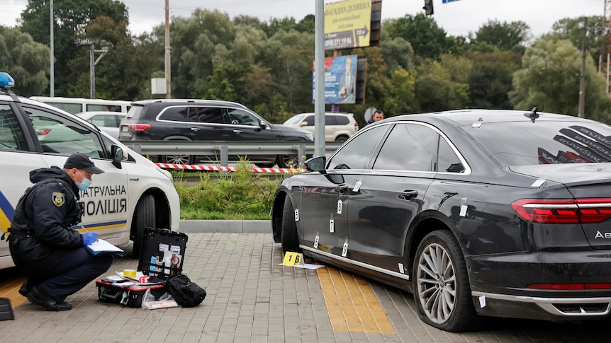 A police officer looks at bullet holes in the side of a black car