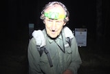 An older man wearing a torch on his head and a backpack