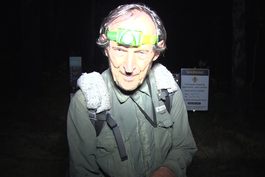 An older man wearing a torch on his head and a backpack