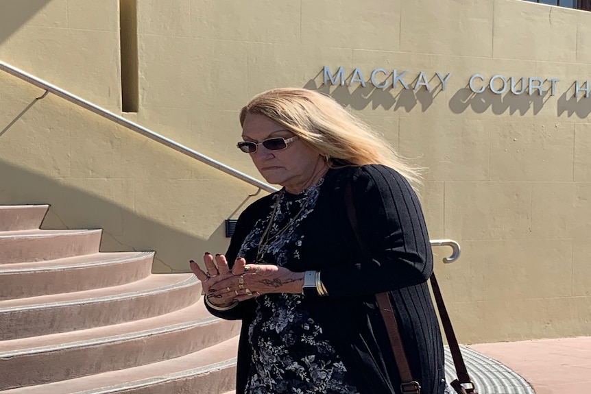 Frau mit langen blonden Haaren und Sonnenbrille geht am Mackay Court House vorbei. 