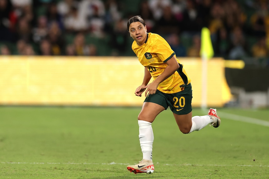 A woman in a yellow soccer shirt runs onto the pitch.