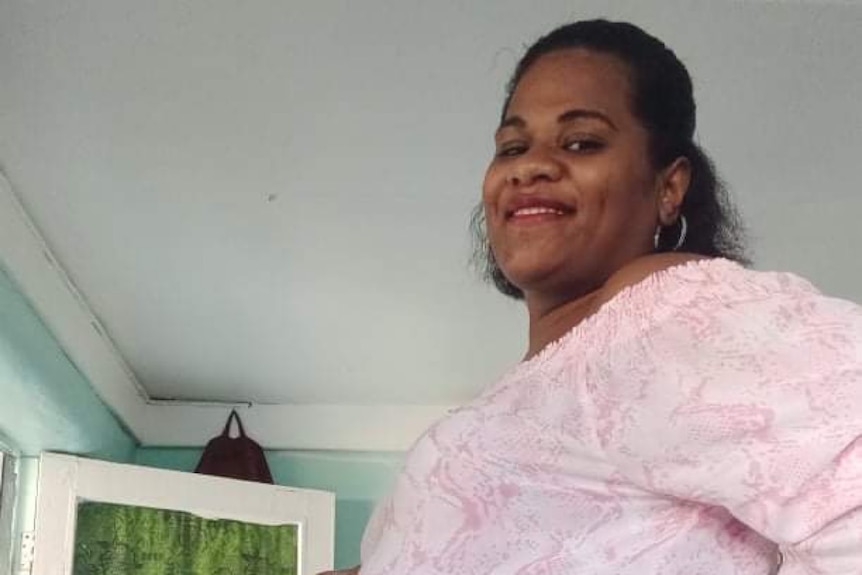 Pregnant woman in white shirt smiles at camera.