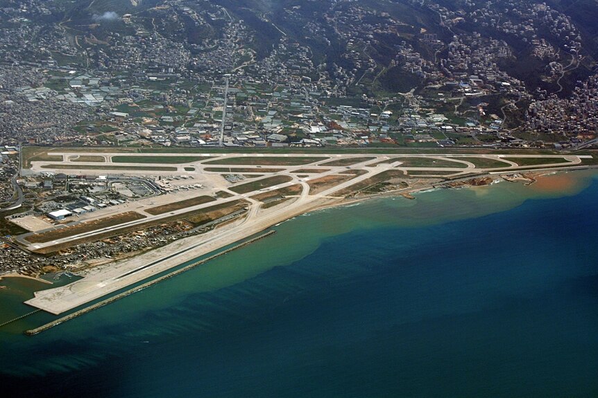 You view an aerial photo of Beirut Airport's three long runways up against a topaz sea and cityscape climbing up nearby hills.