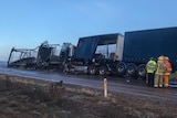Emergency service workers stand on a road beside two B-Double trucks
