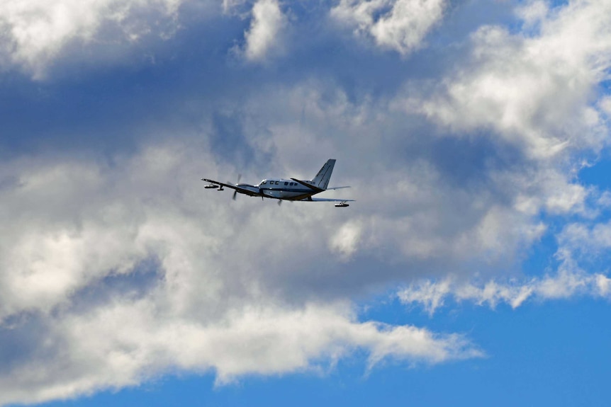 A plane in the sky with clouds in the background.