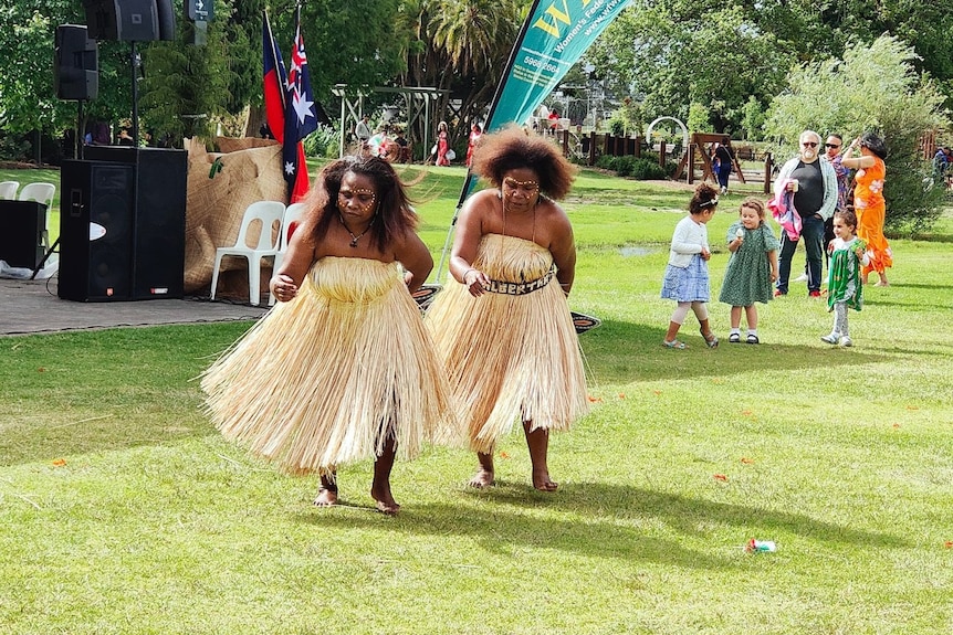 Two women wear traditional Papua New Guinean dress and dance at an event.