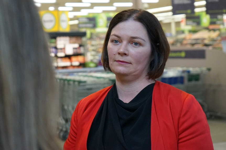 A lady with a brown bob haircut and wearing a red jacket speaks to a person.