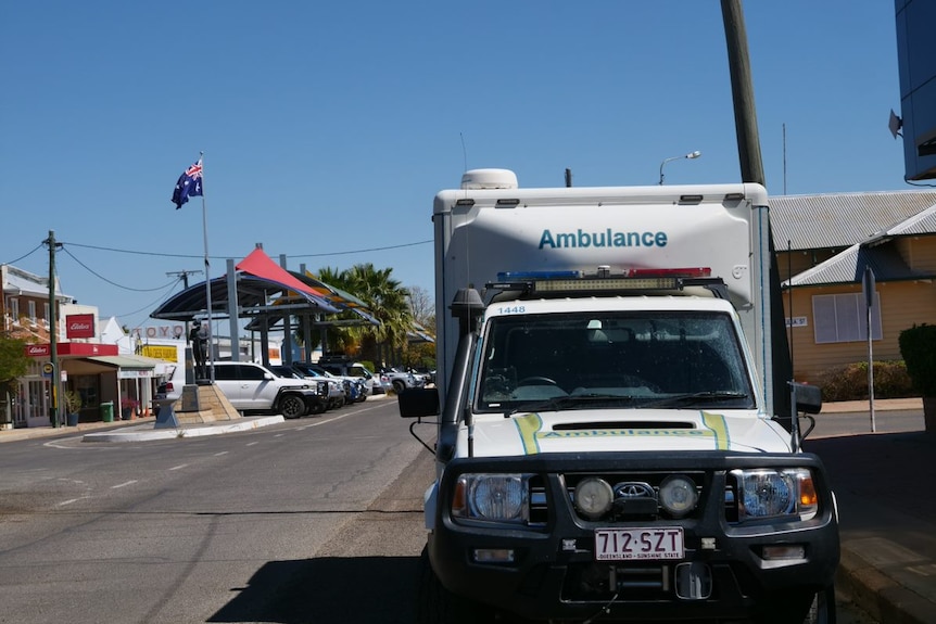 An ambulance parked on a country street with an Australian flag flying in the background.