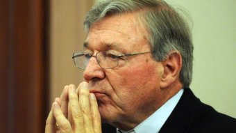 George Pell presses his hands together in front of his face as he sits in a courtroom.