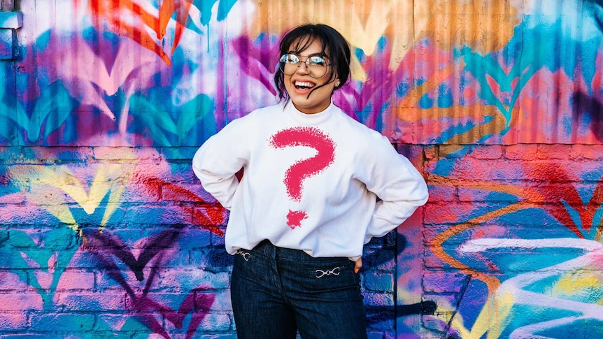 Fashionista standing against wall with question mark t-shirt, representing the search for a personal style/fashion aesthetic