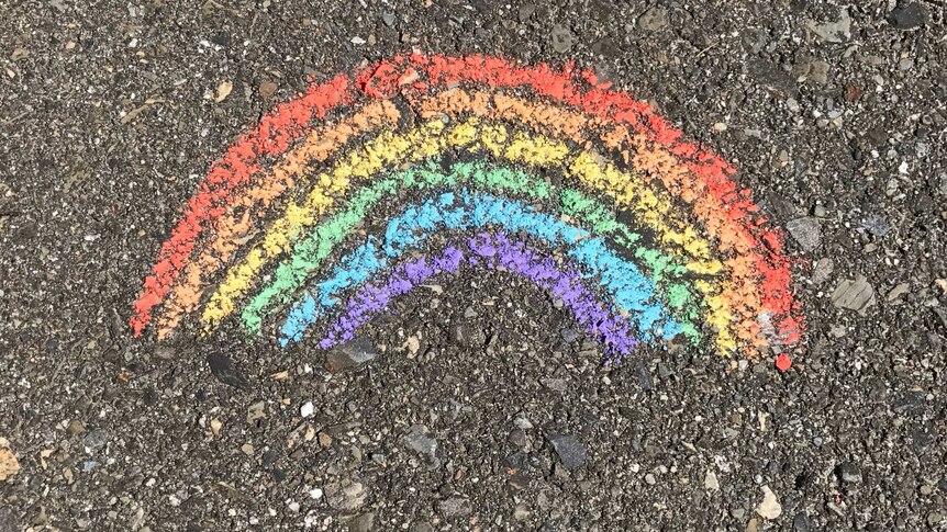 Different coloured chalk is used to draw a rainbow on the pavement