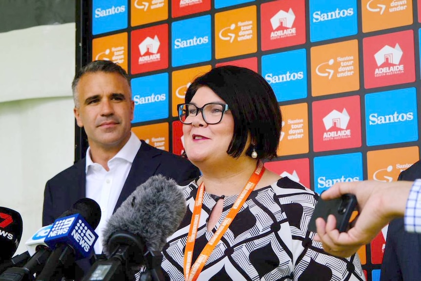 A man and woman stand in front of a colourful backdrop for a press conference