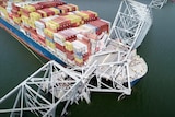 An image of a very large cargo ship with a collapsed bridge sitting over its stern. Some parts of the bridge are submerged.