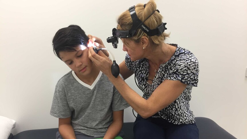 A nurse looks in the ear of a 10-year-old boy using equipment.