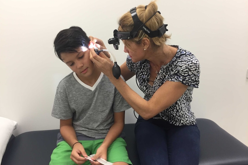 A nurse looks in the ear of a 10-year-old boy using equipment.