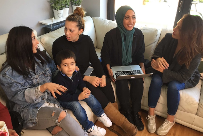 Four women and a toddler sit on a couch