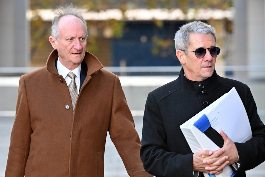 The two men walk outside in winter coats, Drumgold carrying paperwork.