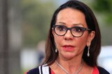Linda Burney, wearing a red, white and navy striped shirt, speaks to reporters. Microphones are being held up to her face