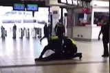 A grainy still image from a video shows a person on the ground while multiple officers surround and pin them down.