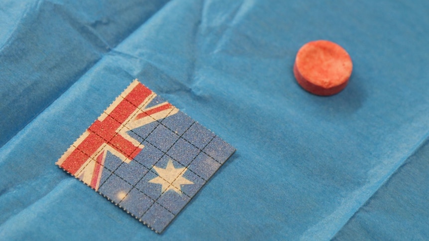A small pill sitting next to a small tab of paper with an Australian flag pattern on it.