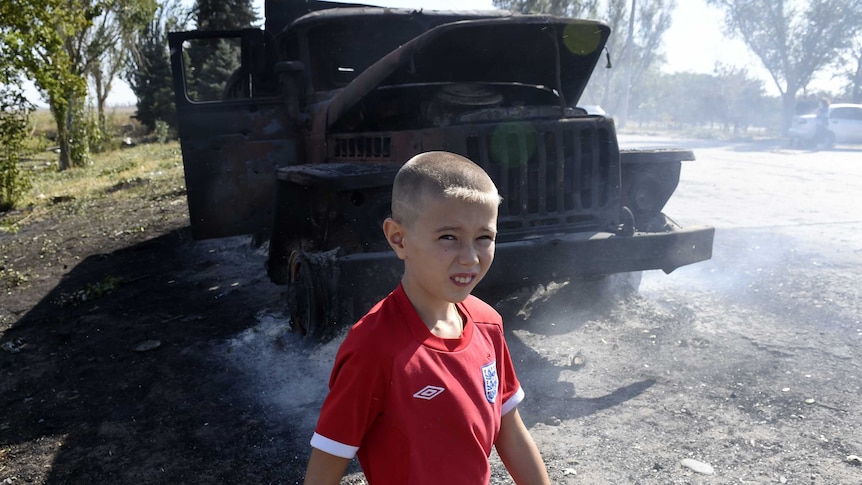 Boy walks by burnt army truck