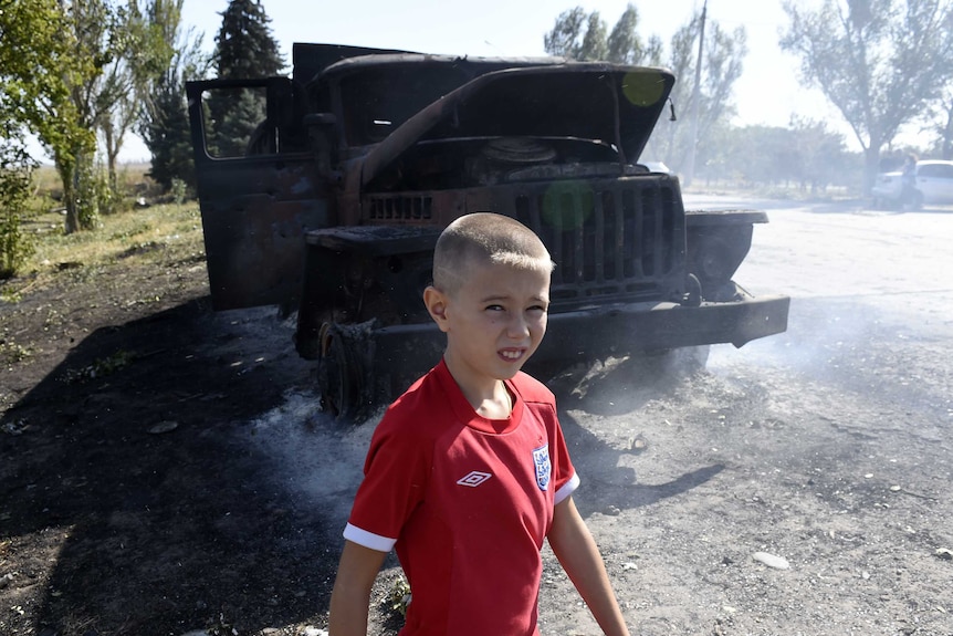 Boy walks by burnt army truck