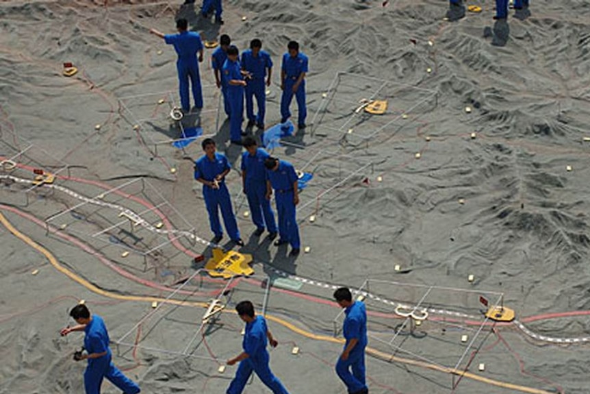 Men in blue overalls are seen walking over a terrain model in Ningxia, China.