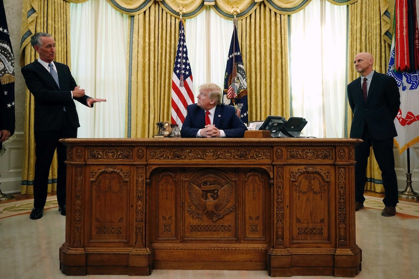Daniel O'Day holds up a hand to Donald Trump who sits at the Resolute Desk.
