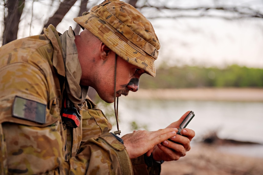a man in army uniform looking closely at a device in his hand