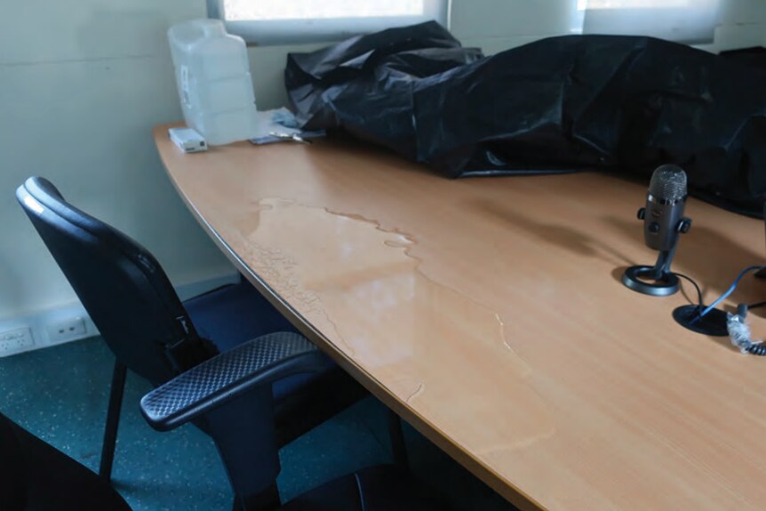A black chair and a wooden desk with a puddle of water on it.