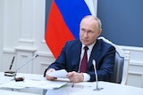 Russian President Vladimir Putin at a desk with a microphone. 