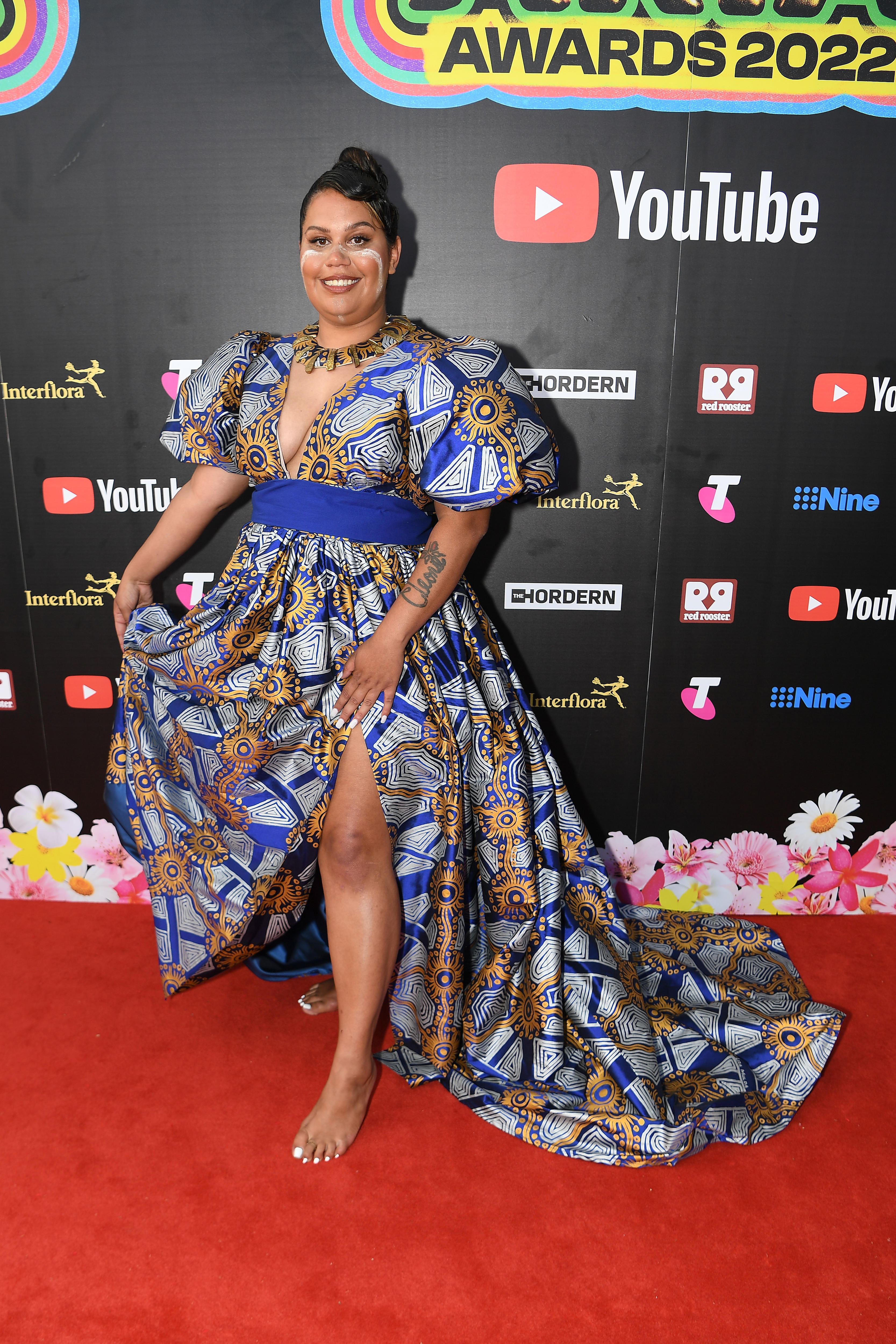 Barkaa wearing a silky purple, white and yellow dress with puffy sleeves, a train and a slit up the side