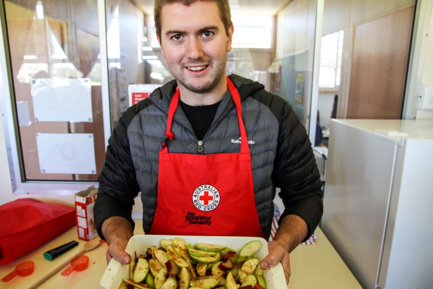 A smiley man proudly holds a dish of rhubarb crumble.