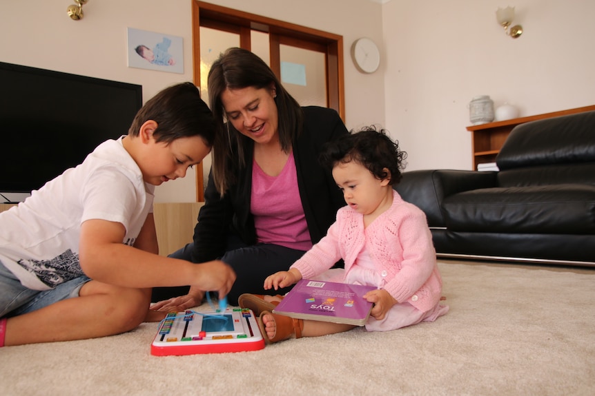 A woman is seen playing with a boy to her left and a girl to her right