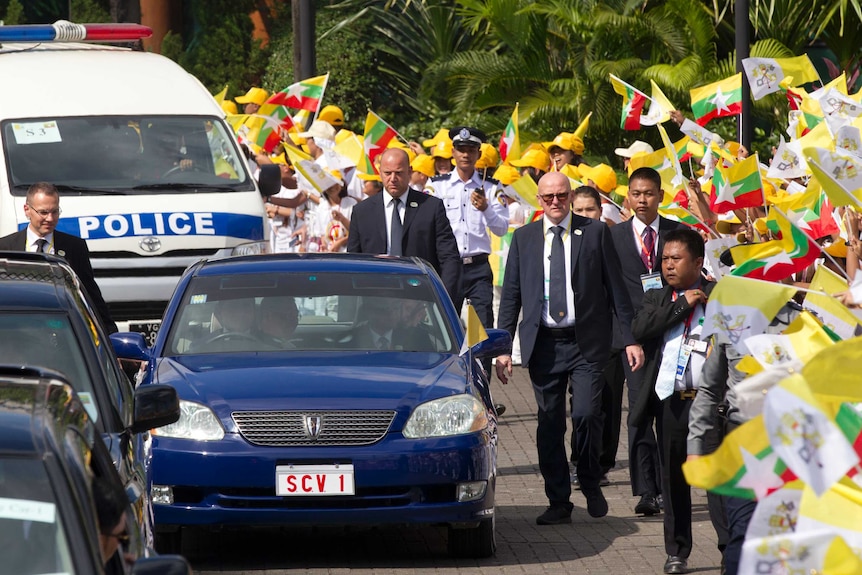 Crowds of people wave flags as the Pope drives past.