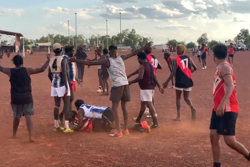 Indigenous footballers play footy on a red gravel oval