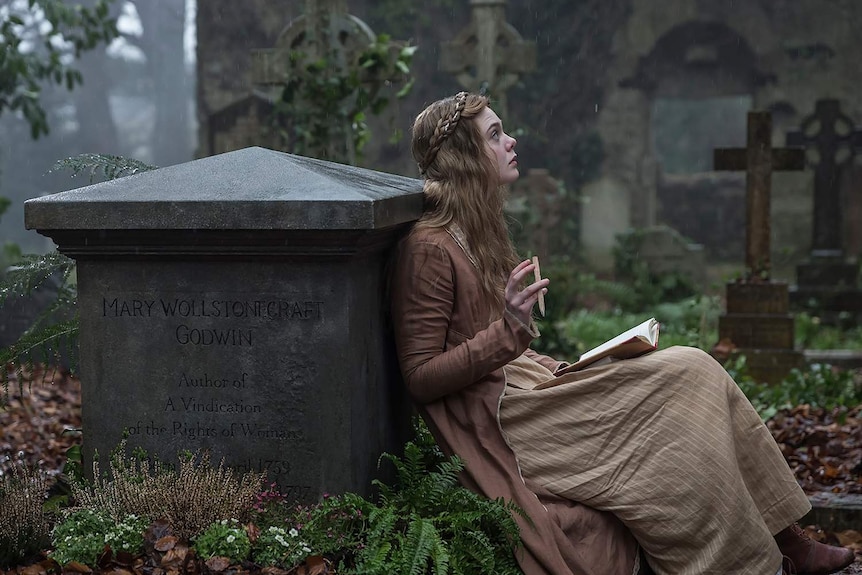 The actor sits in a overgrown, nineteenth century English graveyard, with a pencil and paper in her lap.