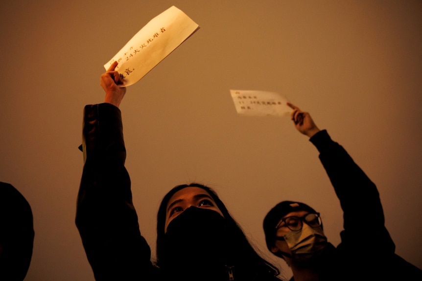 Two people wearing masks hold up blank sheets of paper. 