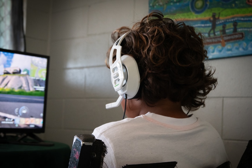 A boy with headphones on sits at a computer.