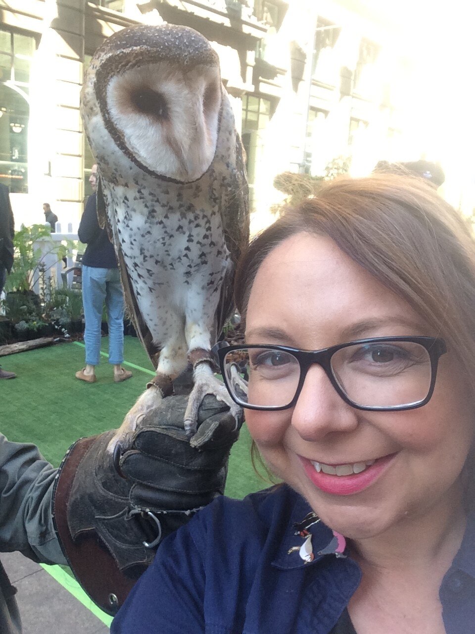 Woman photographed with an owl perched just behind her.