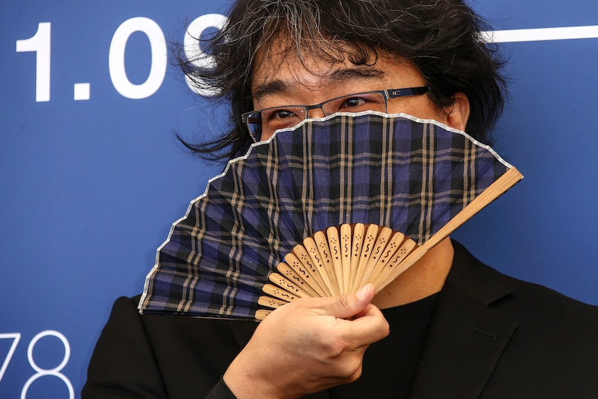 Bong Joon Ho holds a blue tartan hand fan up to his face. 