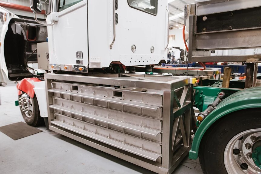 Detalle cercano del paquete de baterías grande instalado en el costado del camión entre las ruedas delanteras y traseras debajo del espacio para los pies de la cabina.