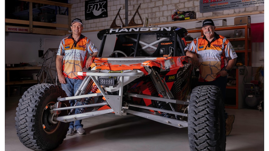 two men stand either side of a bright orange, off-road buggy. They are wearing matching bright orange shirts and black caps