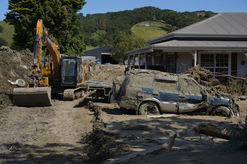 Bulldozer and a car covered in dirt outside a house.