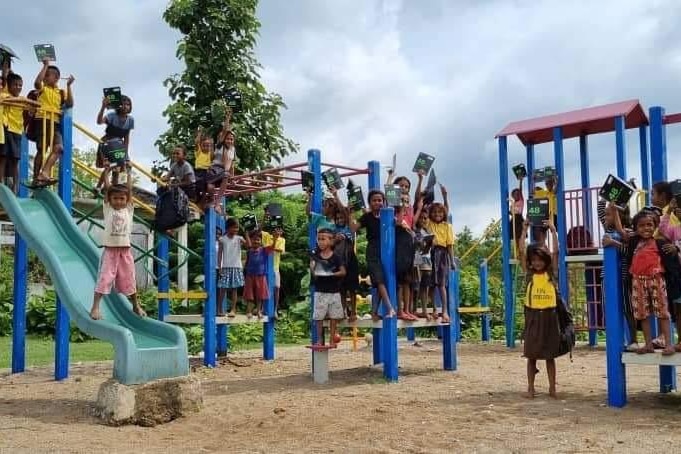 Lots of Timor children climbing and posing on play equipment of slippery slide and bars