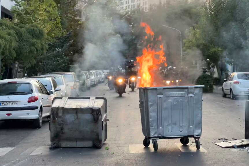  A trash bin is burning as anti-riot police arrive on motorbikes during a protest.