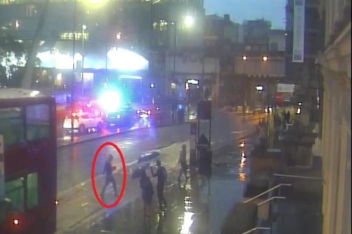 People walk in the rain holding umbrellas crossing over London Bridge.