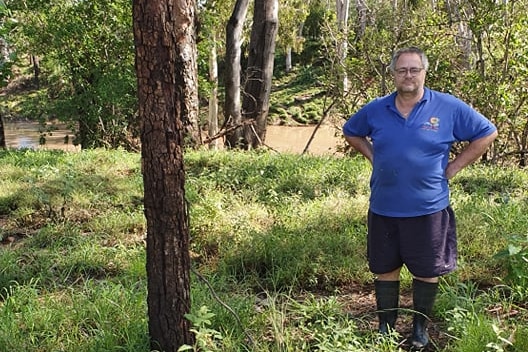 Rodney standing with his hands on his hips, grass and murky creek in background.